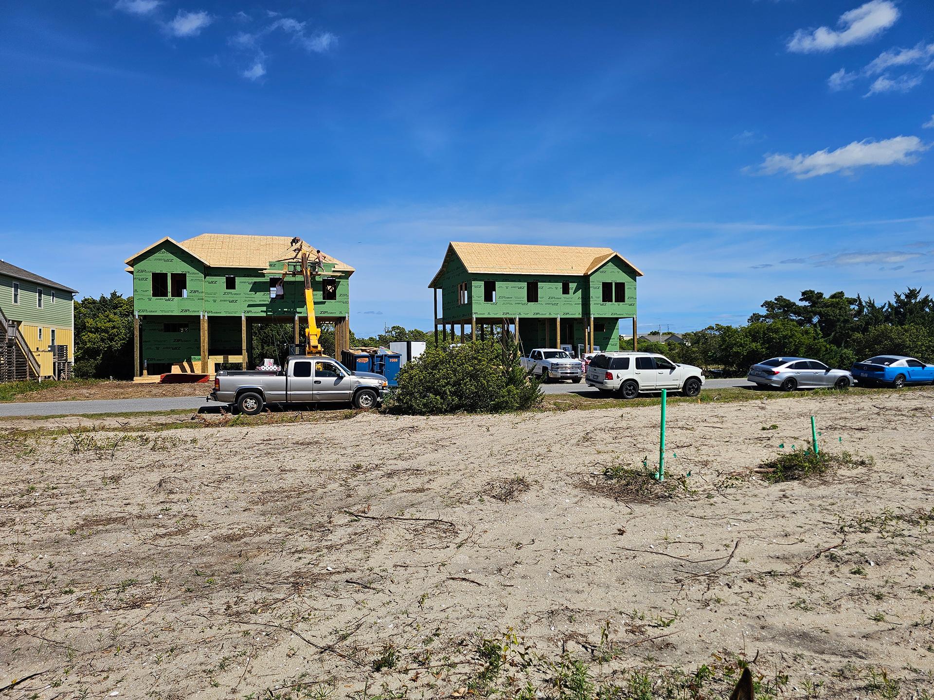 Two green homes under construction on a sandy lot